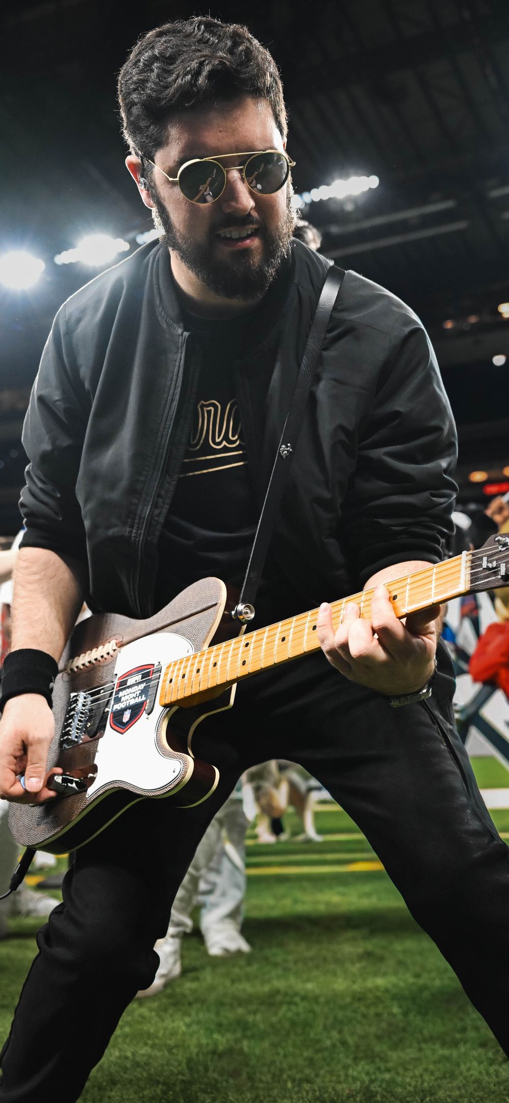 Noah Scott playing the football-leather guitar on the field at Lucas Oil Stadium during Monday Night Football, with the Colts drumline behind him